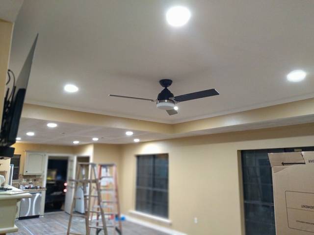 A room mid-remodel with new recessed lights and a ceiling fan, ladders still up